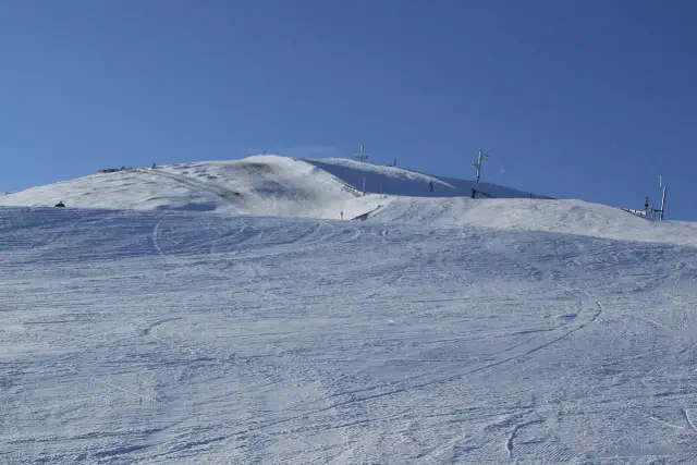 Śnieżne stoki górskie z widocznymi śladami nart. Różne kolory tras narciarskich tworzą wzory na białym puchu.