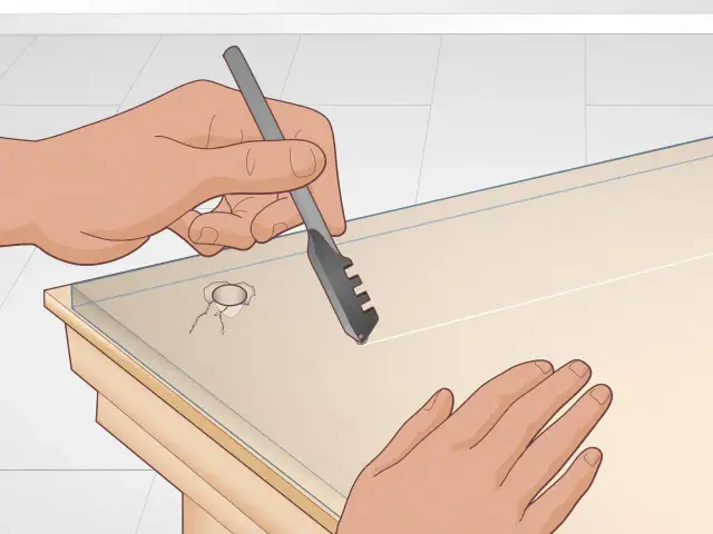 Dwie ręce trzymają narzędzie do cięcia szkła, aby wywiercić otwór w szkle.