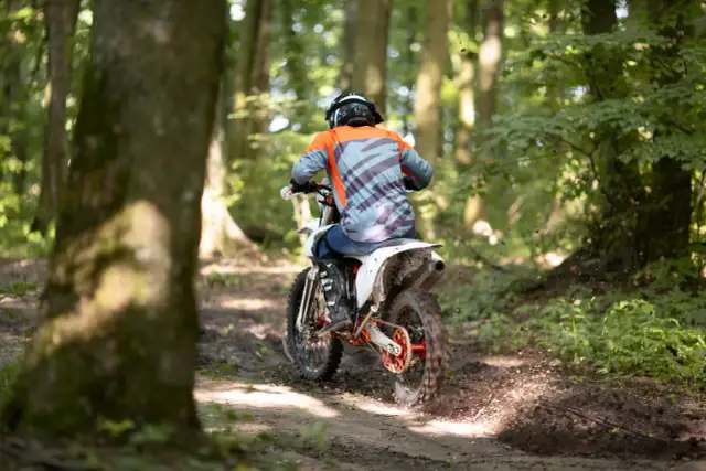 Motocyklista w kasku i kolorowej bluzie pędzi po leśnym torze. Zastanawiasz się, prawo jazdy na crossa od ilu lat jest potrzebne, by poczuć taką wolność?