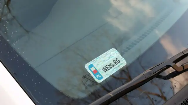 Naklejki na samochód, w tym obowiązkowe naklejki z numerem rejestracyjnym, umieszczone na przedniej szybie.