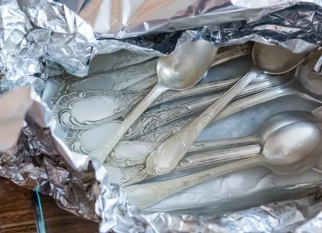 Stos srebrnych łyżek i widelców owiniętych w folię aluminiową.