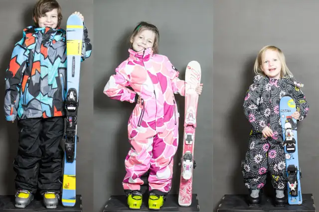 Trójka dzieci gotowa na stok. Chłopiec w kolorowej kurtce i dziewczynki w różowych i czarnych kombinezonach, każde z nartami. Idealne narty dla 3 latka i starszych dzieci.