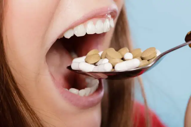 Łyżka pełna tabletek, w tym niesteroidowe leki przeciwzapalne, zbliża się do otwartych ust.