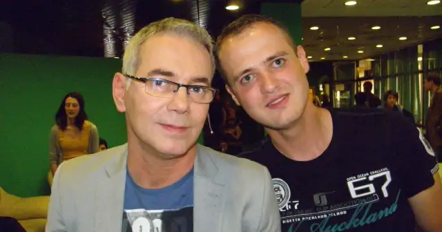 Tomasz Kammel i młody fan pozują do zdjęcia. Tomasz Kammel w szarym garniturze i niebieskiej koszulce, a obok niego młody mężczyzna w czarnej koszulce z napisem "Auckland".