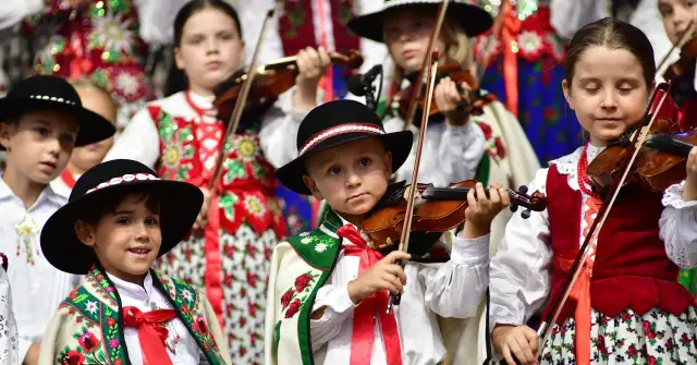 Dzieci w strojach ludowych grają na skrzypcach.
