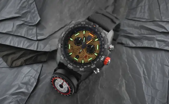 Męski zegarek z tarczą i kompasem, na tle pogniecionej tkaniny.