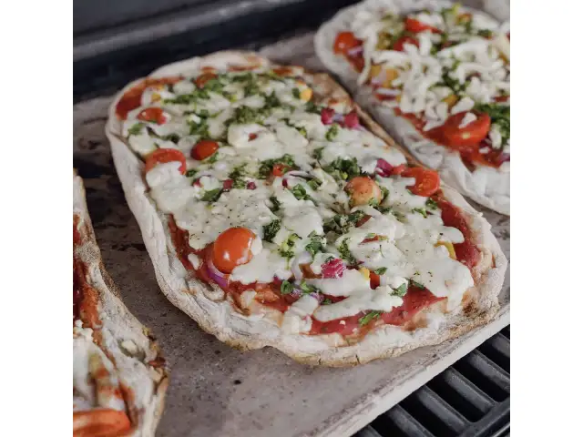 Dwie pizze na kamieniu, z pomidorkami i serem. Dowiedz się, jak przełożyć pizzę na kamień bez łopatki, by uzyskać idealnie chrupiący spód.