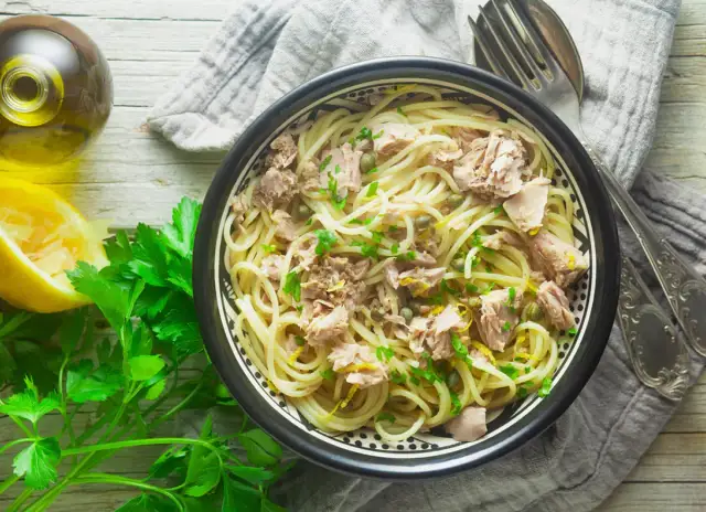 Miseczka spaghetti z tuńczykiem, cytryną i pietruszką na drewnianym stole.