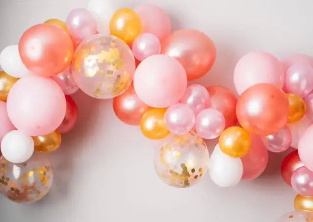 Girlanda z różowych, łososiowych, złotych i białych balonów, w tym kilka z konfetti.