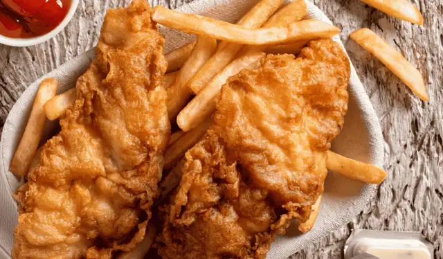 Chrupiący smażony filet rybny z frytkami na drewnianym tle.