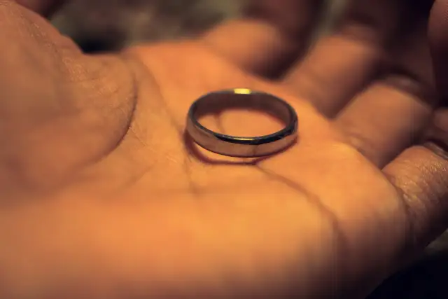 Obrączka spoczywa na otwartej dłoni, w ciepłym, przygaszonym świetle.