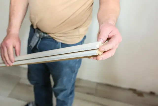 Dłoń trzymająca dwie listwy sufitowe z widocznymi cięciami pod kątem.