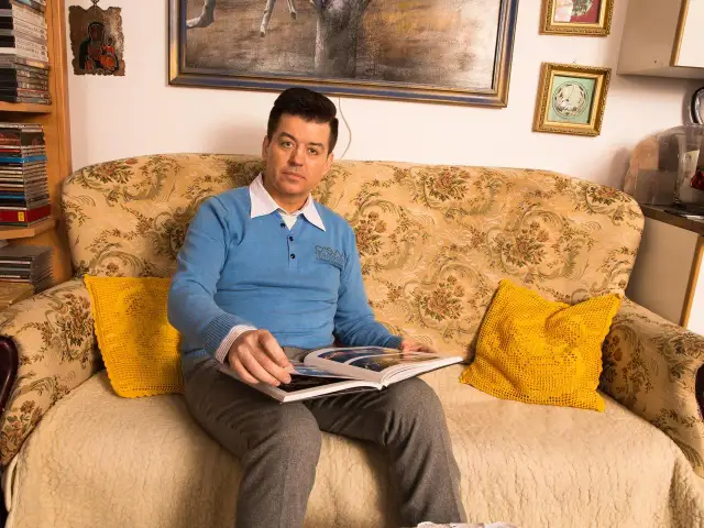 Mężczyzna w niebieskim swetrze siedzi na kanapie, przeglądając książkę. Może to być fragment jego życiorysu, witold matulka.