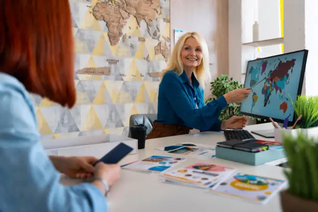 Kobieta w biurze wskazuje na mapę świata na monitorze komputera.