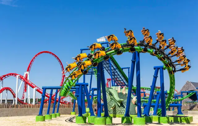 Kolejka górska Hyperion z żółtymi wagonikami na zielonym torze, w tle czerwona kolejka.