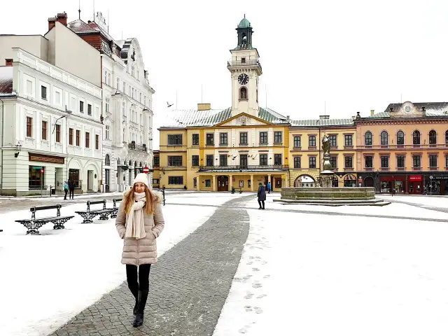 Zimowy spacer po Rynku w Cieszynie. Kobieta w ciepłym ubraniu przemierza ośnieżony plac, podziwiając zabytkowe kamienice i ratusz. Idealny pomysł na cieszyn w jeden dzień.