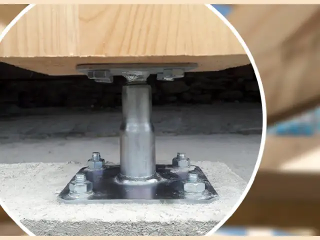 Metalowa kotwa do słupa drewnianego zamontowana na betonowym fundamencie.