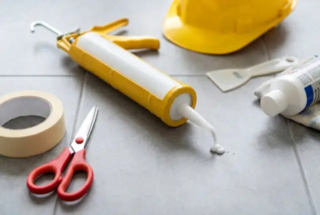 Pistolet do silikonu, nożyczki, taśma, żółty hełm i środek do usuwania silikonu.