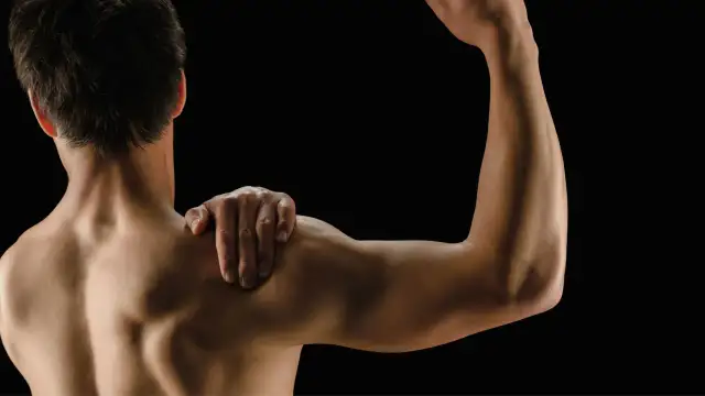 Mężczyzna z ręką na ramieniu, pokazujący umięśnione plecy i biceps. Białko po treningu wspiera regenerację mięśni.