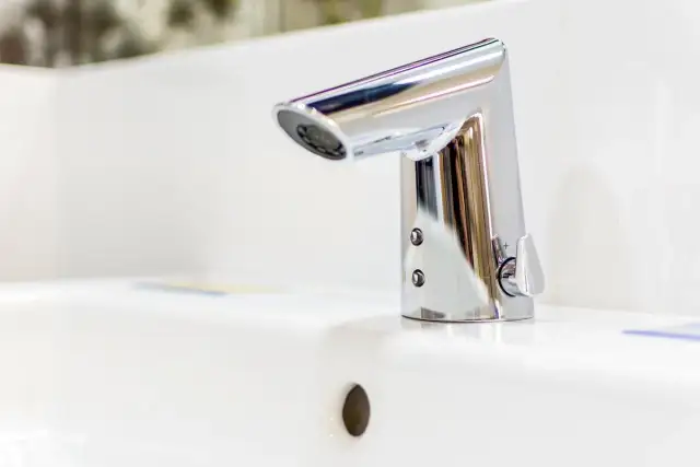 Elegancka bateria umywalkowa z korkiem, wykonana z chromowanego metalu, lśni na białej ceramice.