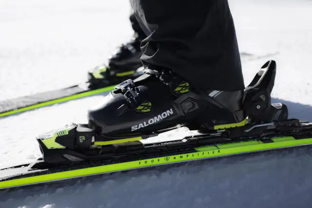 Czarny but narciarski Salomon z neonowo-zielonymi akcentami, idealny dla narciarzy z szeroką łydką, gotowy do zjazdu.