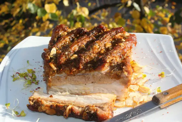 Pyszny boczek pieczony w rękawie, z chrupiącą skórką i soczystym mięsem, podany z kiełkami i plasterkami czosnku.