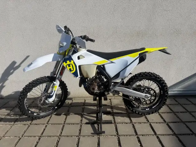 Motocykl Husqvarna WRE 125 na stojaku, biało-żółty, z logo Husqvarna.