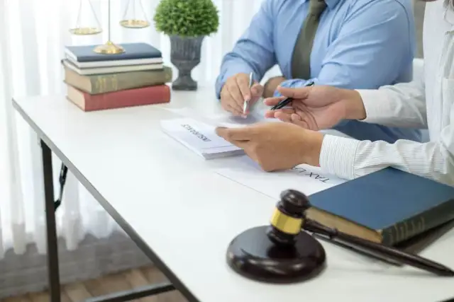 Dwóch prawników przy biurku z dokumentami, książkami i młotkiem sędziowskim.