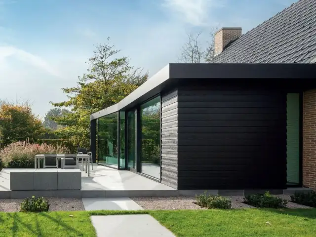 Nowoczesny dom z czarną elewacją drewnianą i dużymi oknami, otoczony ogrodem.
