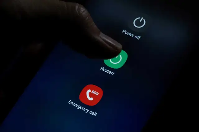 Palec naciska przycisk "Restart" na ekranie telefonu, co może pomóc, gdy zastanawiasz się, jak przywrócić poprzednie ustawienia telefonu.
