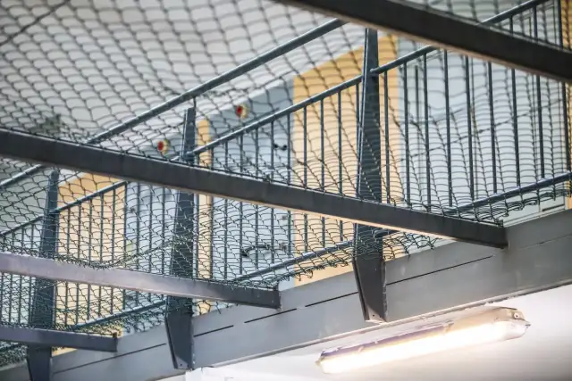 Siatka ochronna i balustrady wewnątrz budynku, widoczna jarzeniówka.