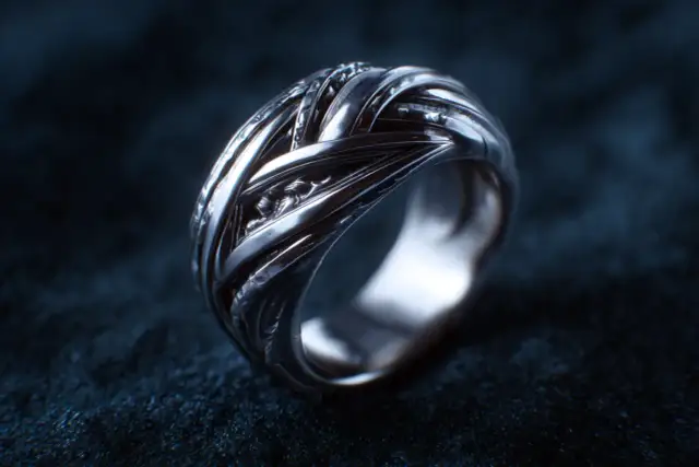 Srebrny pierścionek o plecionym wzorze na ciemnym tle.