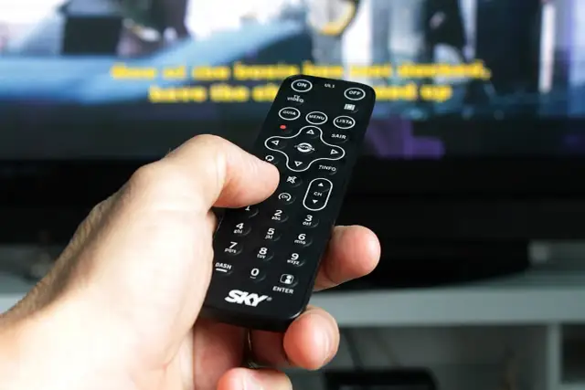 Dłoń trzyma pilot, by jak wyszukać kanały w telewizorze. Widoczne przyciski MENU, LISTA i CH.