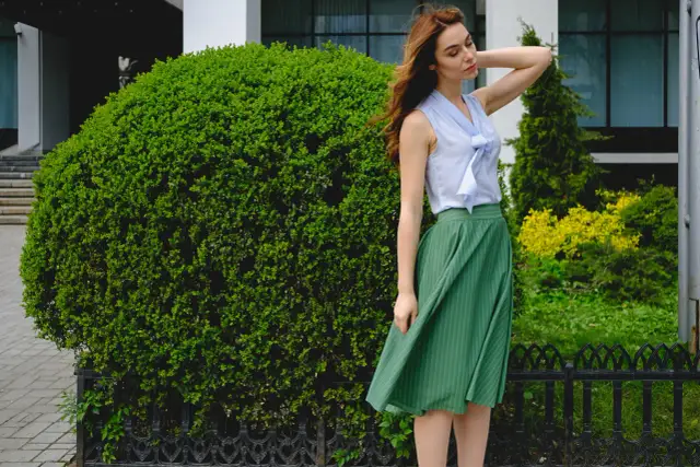 Elegancka stylizacja: błękitna bluzka z kokardą i zielona spódnica w paski. Idealna odpowiedź na pytanie: jaka bluzka do zielonej spódnicy.