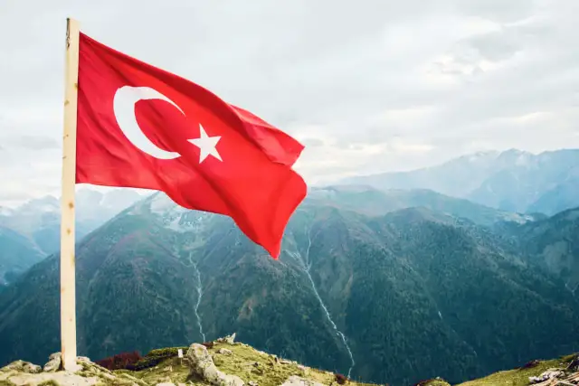 Turecka flaga powiewa na tle górskich krajobrazów. Zastanawiasz się, ile trwa lot do Turcji?