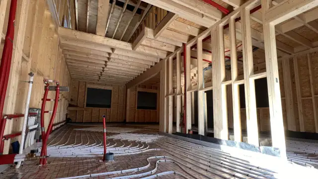 Budowa domu szkieletowego: widok wnętrza z instalacją ogrzewania podłogowego i drewnianą konstrukcją.