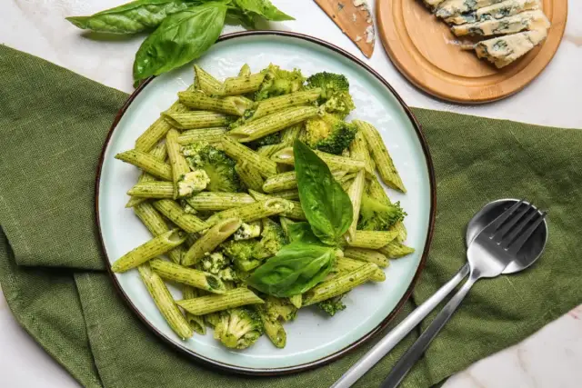 Penne z brokułami i serem gorgonzola w sosie pesto, udekorowane listkami bazylii. Idealne danie dla miłośników makaronu.