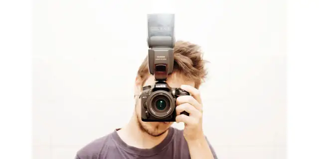 Mężczyzna z aparatem Nikon i lampą błyskową na gorącej stopce. Pokazuje, jak używać lampy błyskowej do lepszego oświetlenia.