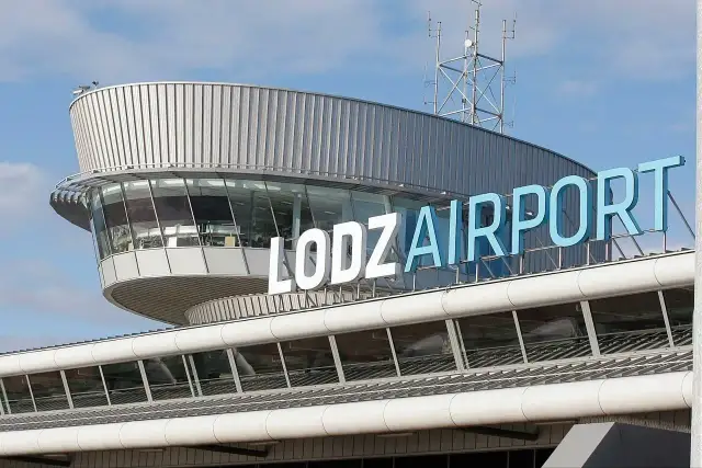 Budynek lotniska w Łodzi z napisem "ŁÓDŹ AIRPORT" na niebieskim niebie.
