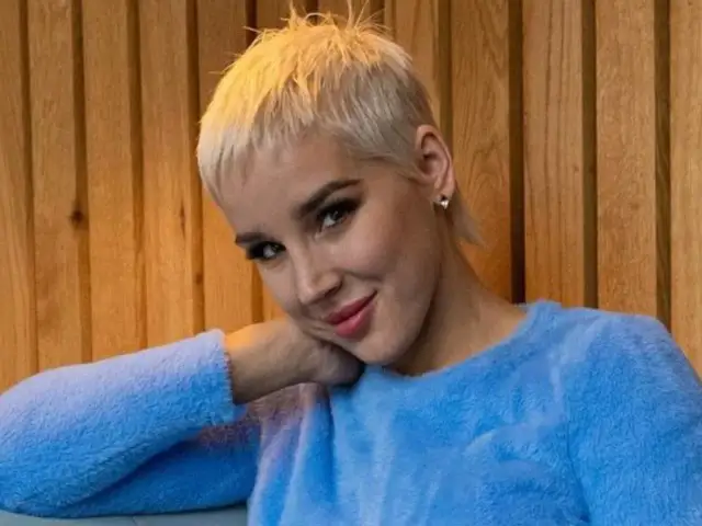 Kobieta z krótkimi blond włosami w niebieskim swetrze opiera głowę na dłoni.