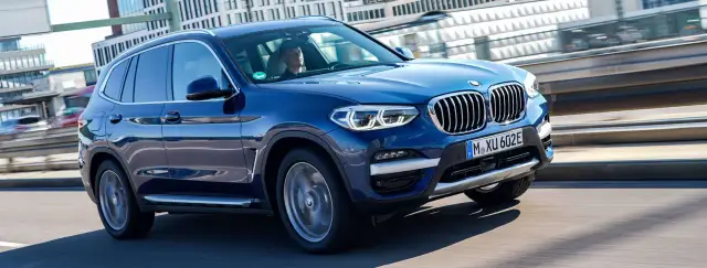 Niebieskie BMW X3 w ruchu miejskim. Zastanawiasz się, ile kosztuje BMW X3? Ten model wygląda na nowy i luksusowy.