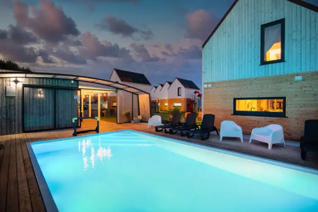 Klimatyczne noclegi nad morzem: basen, leżaki i nowoczesne domki w blasku wieczornego nieba.