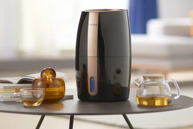 Elegancki nawilżacz ewaporacyjny Philips, obok szklanej filiżanki z herbatą i ozdobnej buteleczki. Czy do nawilżacza ewaporacyjnego można dodać olejek?