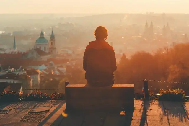 Osoba siedzi na ławce, patrząc na miasto w zachodzącym słońcu. Może to być moment refleksji nad zespołem pomijania stronnego.