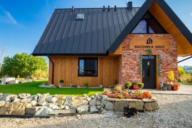 Nowoczesna bacówka w Białce Tatrzańskiej, "Bacówka Dolly", z drewnianą i ceglaną elewacją, otoczona ogrodem z kamiennym murkiem i psem.