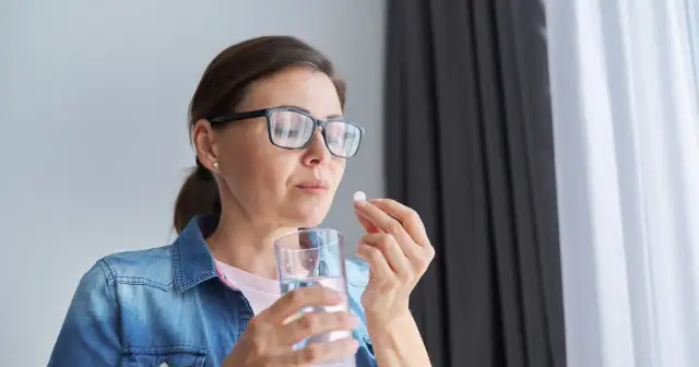 Kobieta w okularach bierze tabletkę, zastanawiając się nad mysimba skutki uboczne.