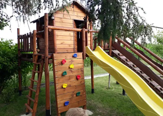 Drewniany domek na placu zabaw ze zjeżdżalnią, ścianką wspinaczkową i drabinką.