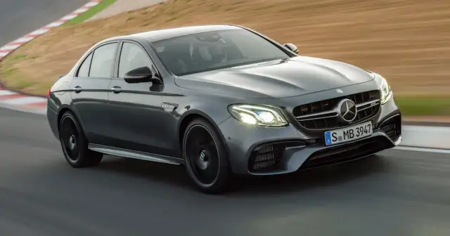 Szary Mercedes-Benz E63 AMG na torze wyścigowym, z kierowcą w kasku za kierownicą.