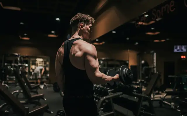 Mężczyzna ćwiczy biceps z hantlem w siłowni. To dowód, jak crossfit zmienił moje życie, budując siłę i pewność siebie.