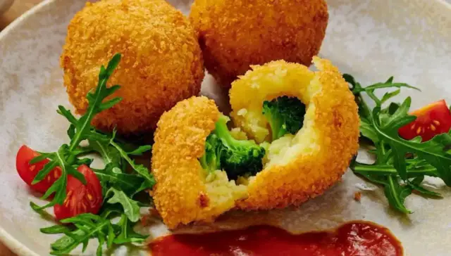 Chrupiące kulki ziemniaczane w panko z brokułami w środku, podane z rukolą i pomidorkami.